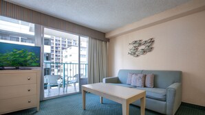 Habitación de hotel con sofá, mesa, televisión y vista a un edificio.