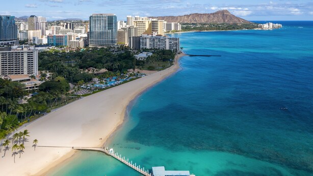 Vista aérea de una ciudad costera con playa, muelle y edificios altos.