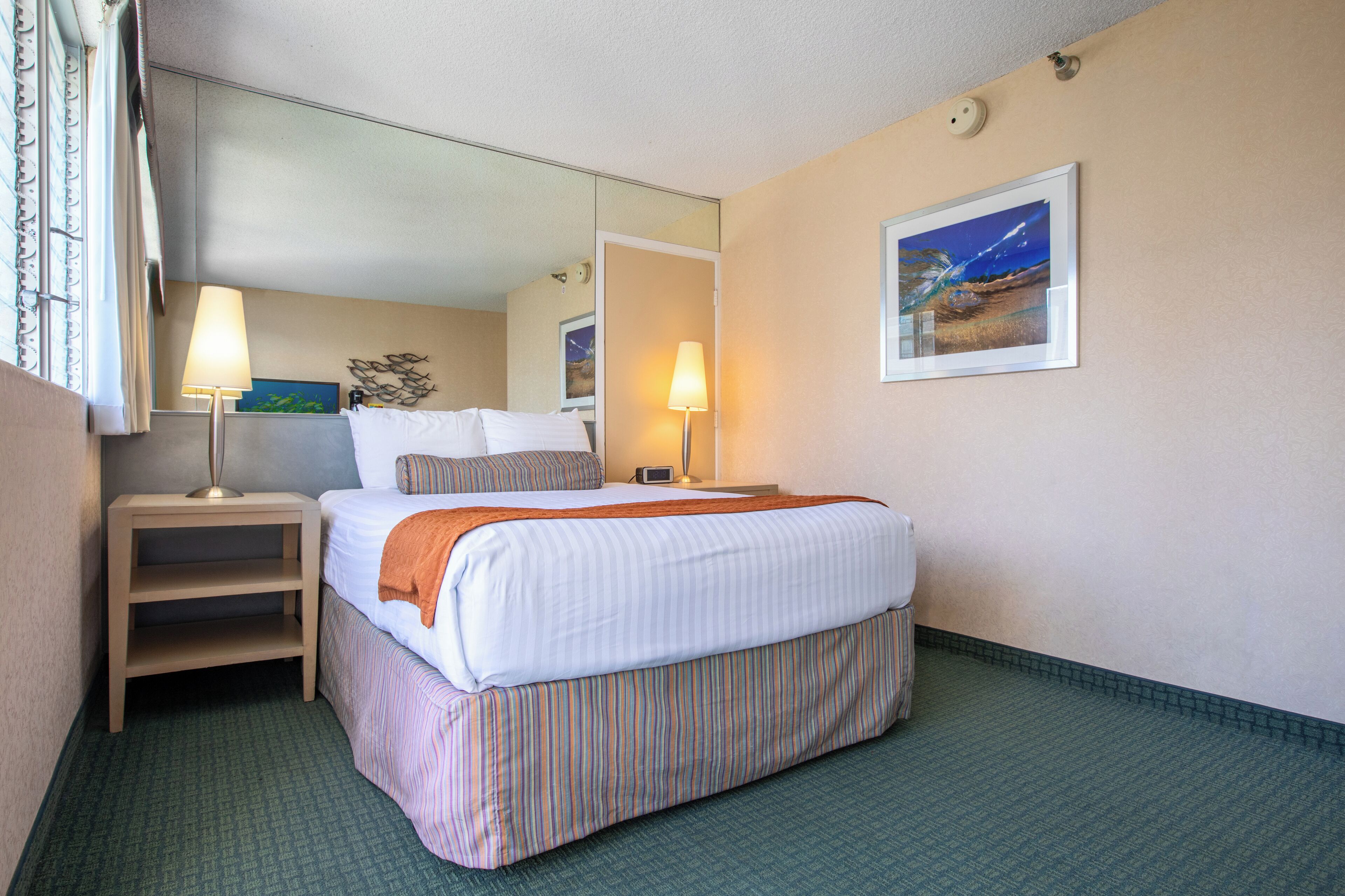 A hotel room with a bed, two bedside tables, a lamp, a painting, and a mirror.