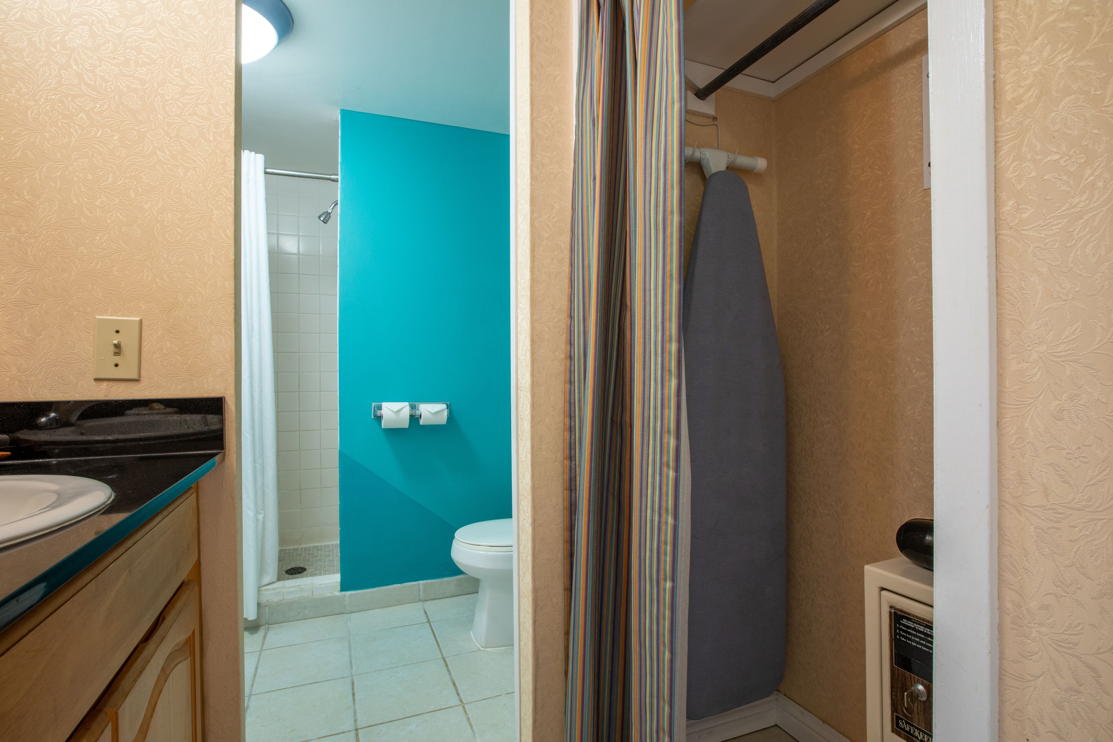 Une salle de bain avec un mur d’accent bleu, un rideau de douche, des toilettes et un lavabo.
