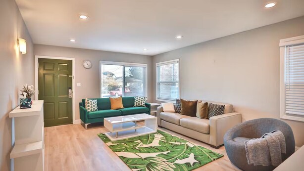 A living room with a green sofa, a white coffee table, and a grey armchair. - Tropical Modern Oasis With Fully Fenced Yard 22409 (Hayward)