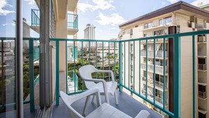 A balcony with two white plastic chairs, a glass door, and a view of surrounding buildings. - Aqua Aloha Surf Waikiki 904 | City View Suite – Pool & BBQ (Honolulu)