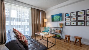 Een moderne woonkamer met een leren bank, een houten salontafel en een blauwe fauteuil. Er hangt een televisie aan de muur en er zijn foto’s van vissen in lijsten.