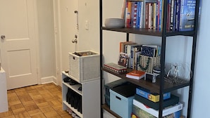 A hallway with a bookshelf containing books and decorative items, a door, and storage bins. - Stylish 1 bedroom apartment, walking distance to Georgetwon (Arlington)