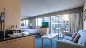A hotel room with a kitchenette, a bed, a TV, a sofa, and a view of the city.
