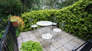 Eine Terrasse mit rundem Tisch und vier Stühlen, umgeben von üppigem Grün.