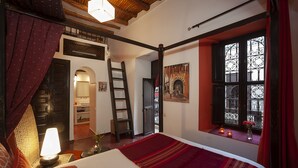 A bedroom with a bed, a nightstand, a lamp, a window with decorative iron bars, and a painting on the wall. - Chambre Limoun (Marrakech)