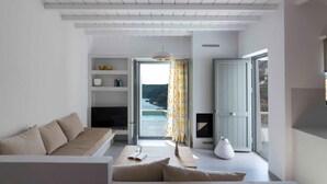 Una sala de estar moderna con un sofá, una mesa de centro y una chimenea. Hay un ventanal con vistas al mar y una puerta que da al exterior.