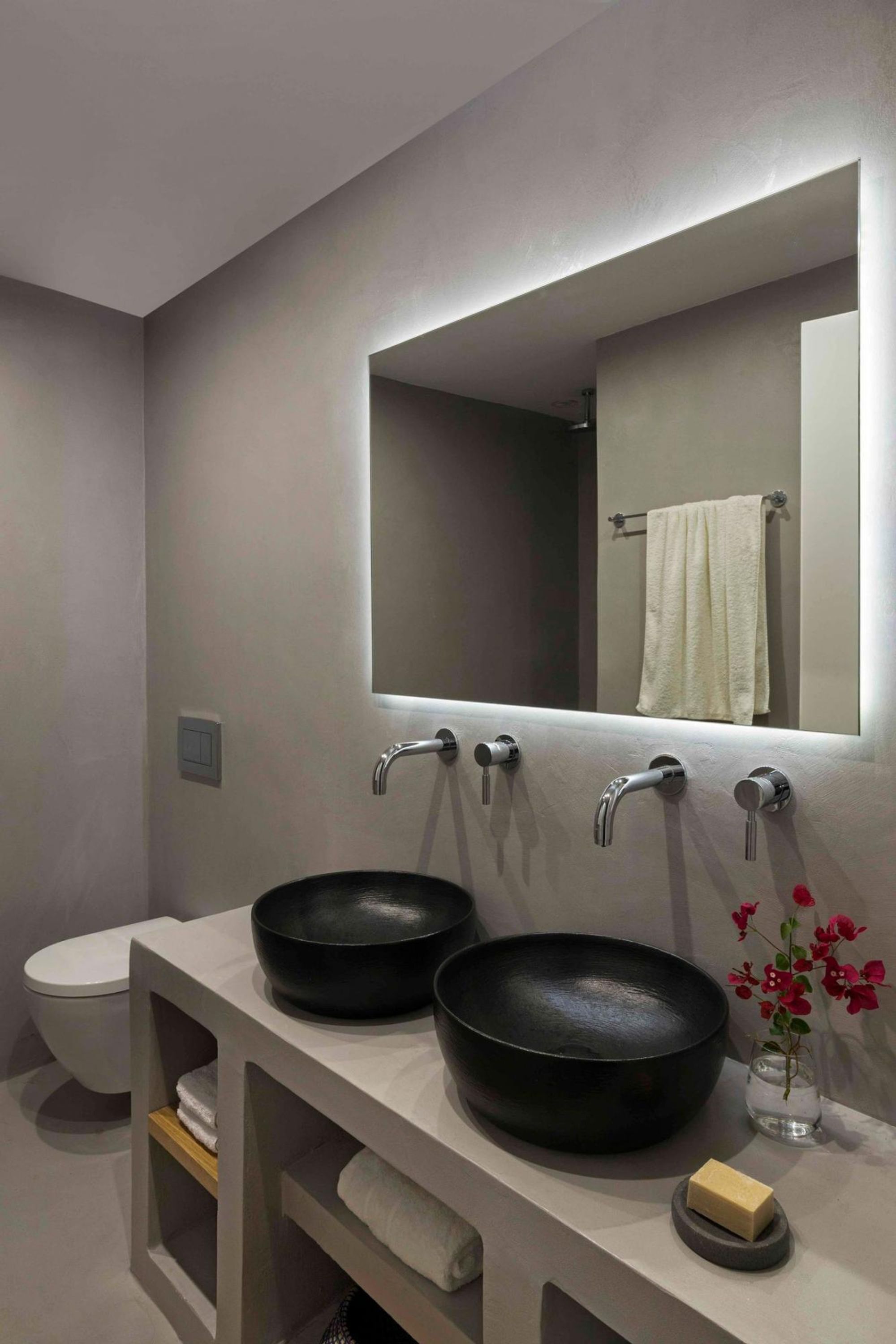 Un baño moderno con dos lavamanos negros, un espejo grande y un toallero blanco.