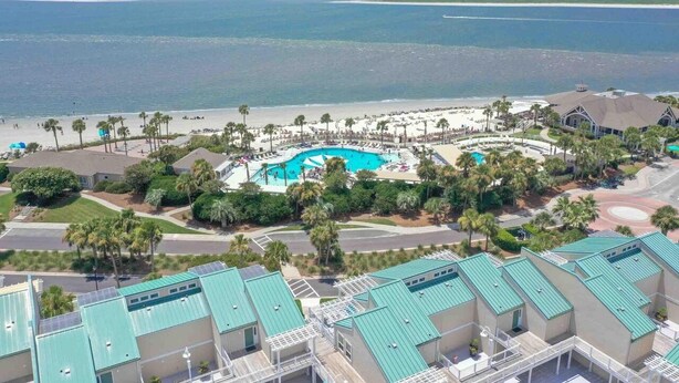 Een resort met een groot zwembad, toegang tot het strand en meerdere gebouwen met groene daken.
