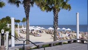 Een strandresort met ligbedden, parasols, een houten looppad en palmbomen.
