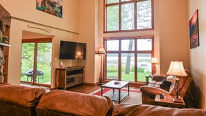 A spacious living room with a large window, a flat-screen TV, leather sofas, and a coffee table. - Perfect Northwoods Retreat (tomahawk)