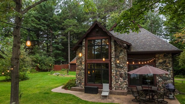 A rustic cabin with a stone exterior, large windows, and a patio area with outdoor seating. - Perfect Northwoods Retreat (tomahawk)