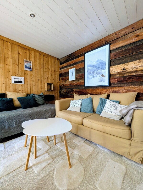Ett mysigt rum med en väggpanel av trä, en soffa, en mindre divansoffa och ett runt bord.