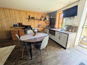 En inredning med träpanel, ett matbord, stolar, ett köksområde och en tv.