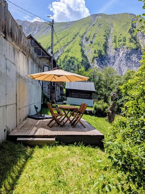 A wooden deck with a table and chairs, a large umbrella, and a view of green hills and a mountain in the background.