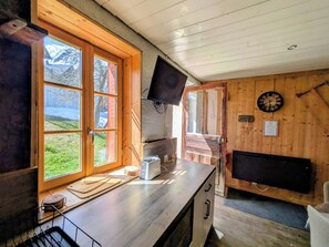 A wooden cabin interior with a large window, a flat-screen TV, a clock, and a fireplace.