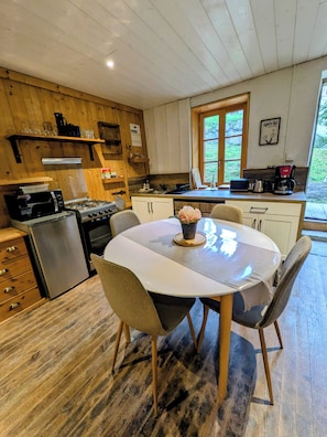 A wooden interior with a kitchen area, dining table, chairs, and a window.