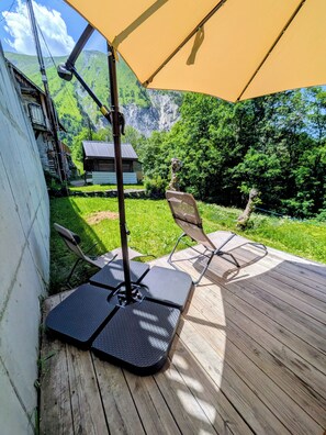 Une terrasse en bois avec un parasol jaune, des meubles d’extérieur et une vue sur un paysage montagneux.
