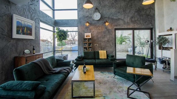 A spacious living room with a large window, a green sofa, a coffee table, and a bookshelf.