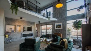 A spacious living area with a large TV, comfortable seating, and a balcony with plants.