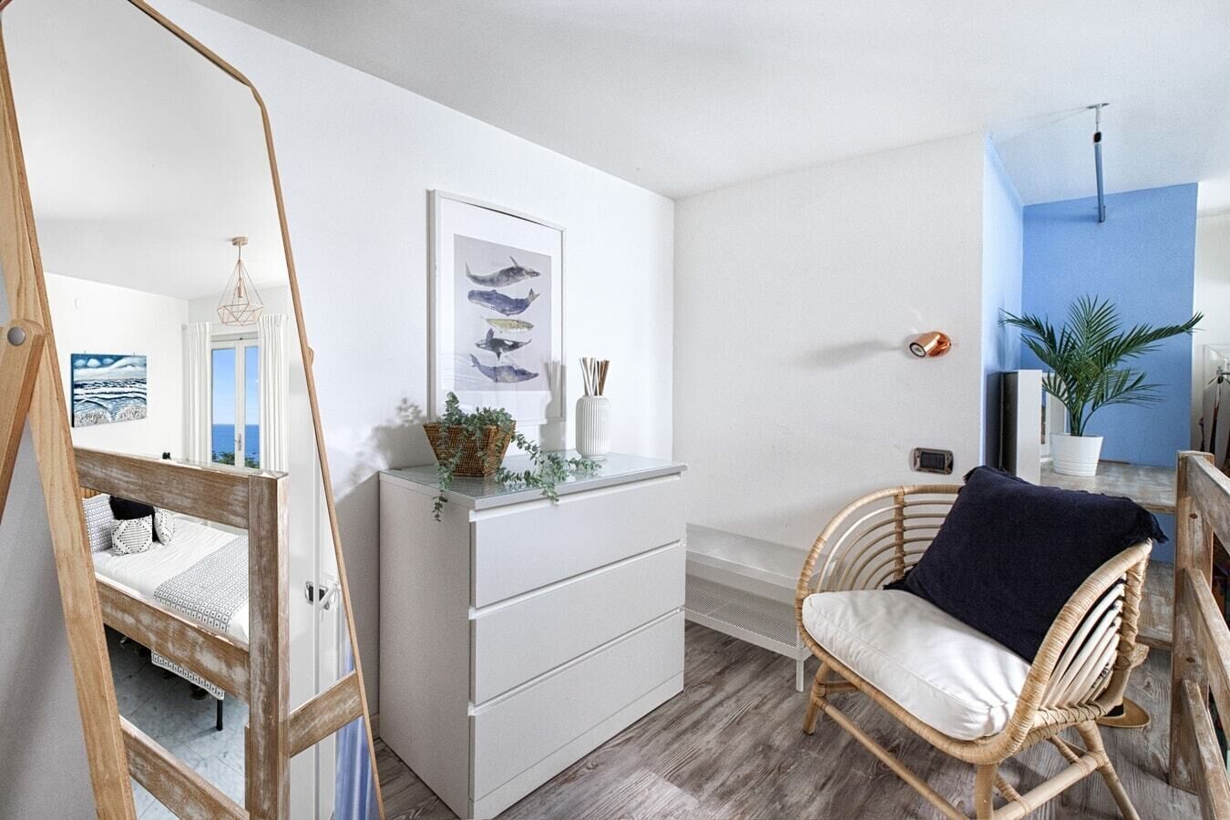 A modern room with a wooden bed, a white dresser, a wicker chair, and a framed picture of fish on the wall.