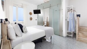 Un dormitorio moderno con cama, televisor, armario y vista al mar.