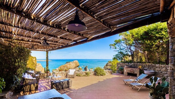 Une terrasse extérieure avec des meubles en osier, une table avec un panier, et une vue sur la mer.