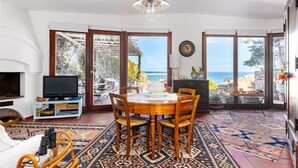 Un coin repas avec une table ronde et des chaises, un téléviseur et une vue sur la mer grâce à de grandes fenêtres.