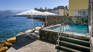 A pool area with steps leading into a clear blue pool, surrounded by stone walls and white umbrellas.