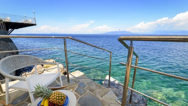 A deck with a table, chairs, and a fruit plate overlooking the sea.