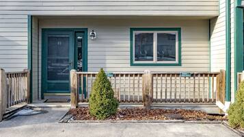 A building with a green door, a window, and a small tree in the front yard.