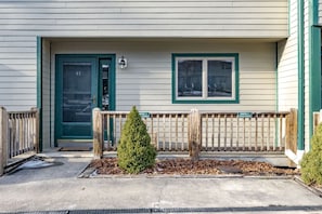 A building with a green door, a window, and a small tree in the front yard.