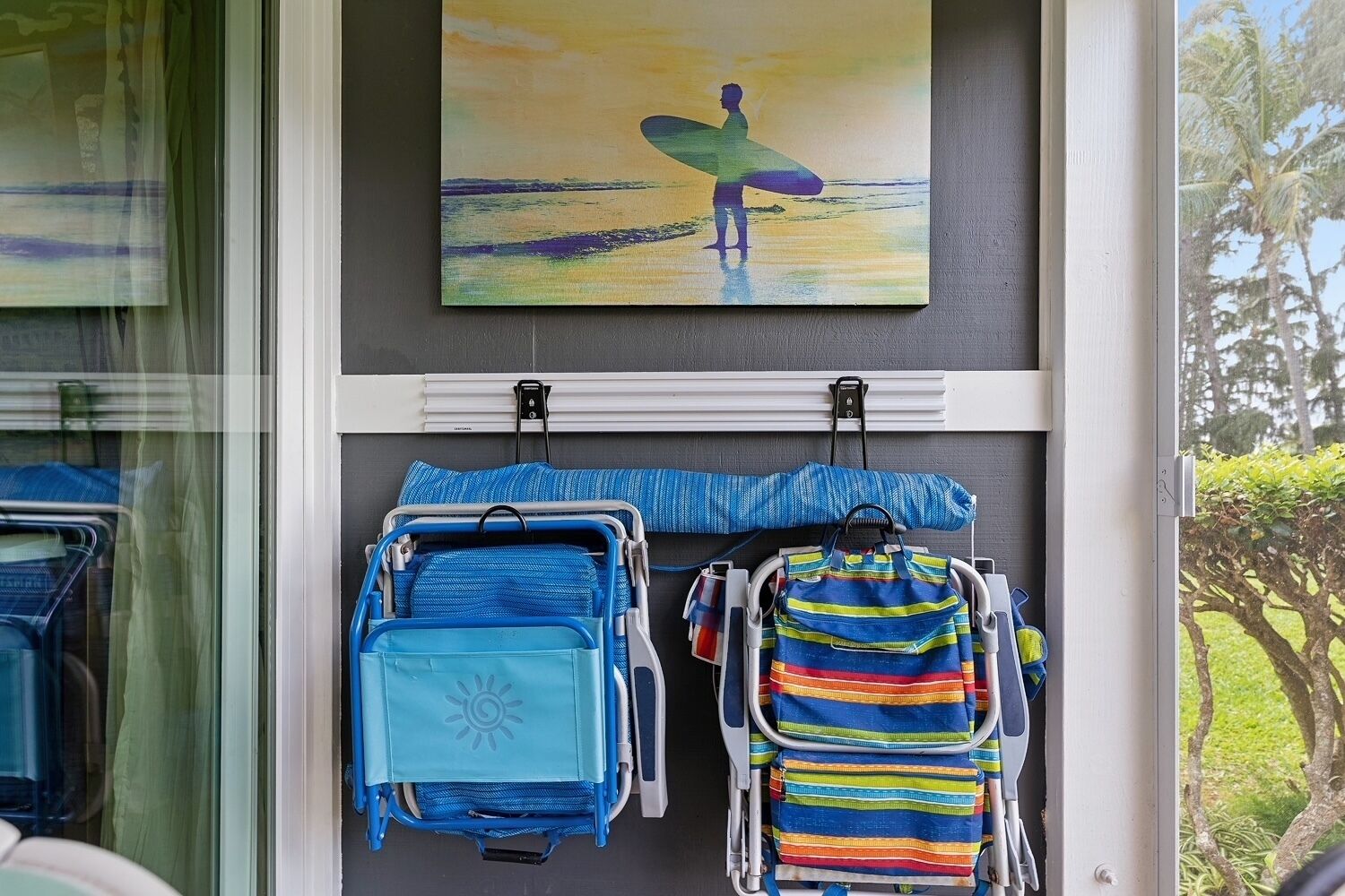 A window with a painting of a surfer and two colorful backpacks hanging on hooks.