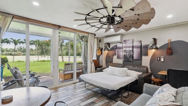 A modern bedroom with a large bed, a ceiling fan, a guitar, and a view of the outdoors. - NEW! RusticLuxe — Fully Custom Boss Cabin at Turtle Bay (Kahuku)