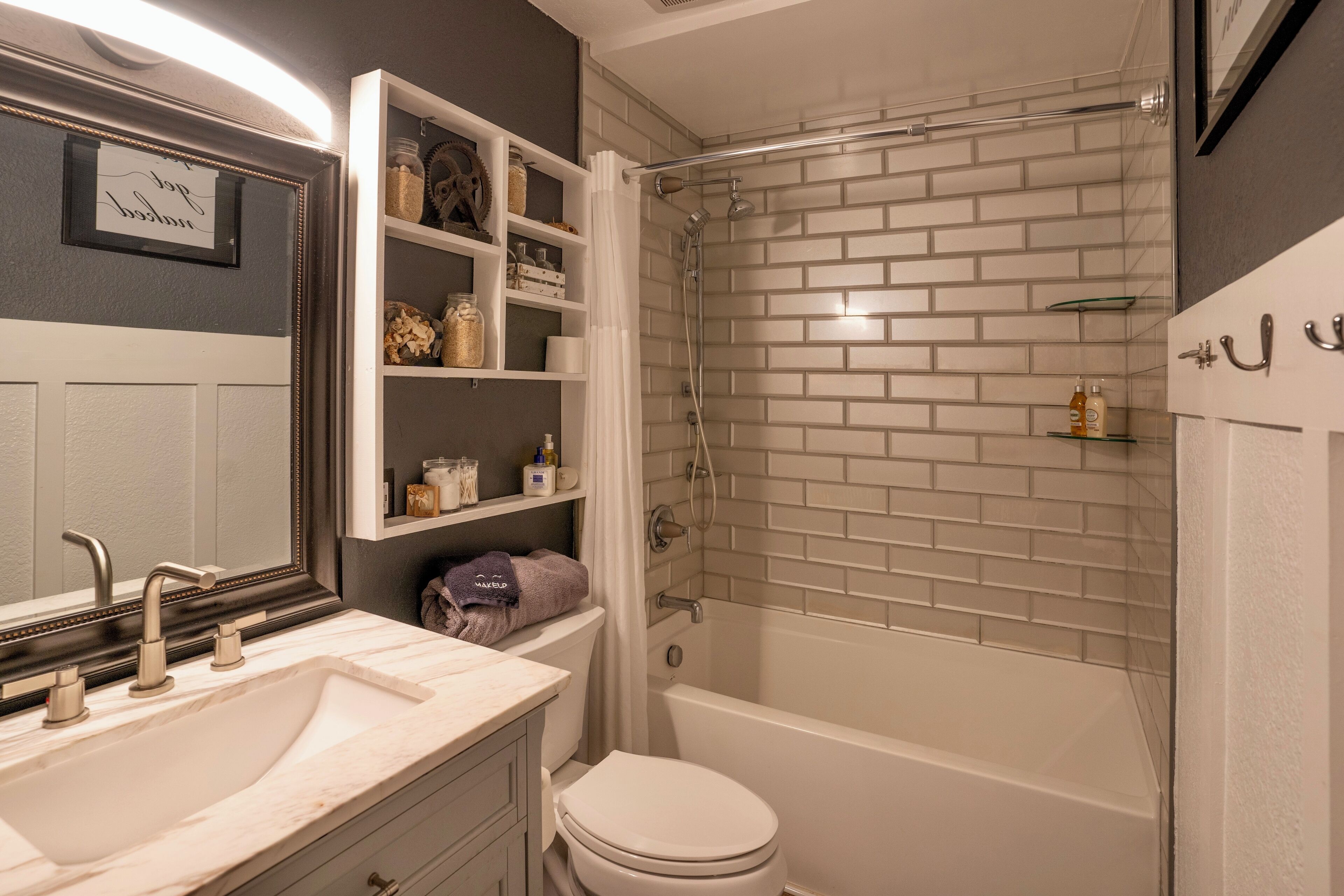 A bathroom with a white sink, mirror, and toilet. There is a shower with a glass door and a bathtub. Shelves with toiletries are visible.