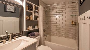 A bathroom with a white sink, mirror, and toilet. There is a shower with a glass door and a bathtub. Shelves with toiletries are visible.