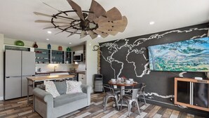 A modern kitchen with a dining area, a grey sofa, and a world map mural. - NEW! RusticLuxe — Fully Custom Boss Cabin at Turtle Bay (Kahuku)