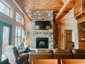 Ein Holzblockhaus-Interieur mit Kamin aus Stein, Ledersofas und einem montierten Fernseher.