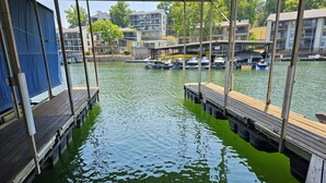 A marina with docked boats and a view of residential buildings in the background. - Lakefront Home with Private Dock, Water Slide, Boat Slip, and Hot tub (Lake Ozark)