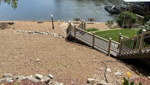 A waterfront view with a dock, a covered seating area, and a grassy area with a pathway. - Lakefront Home with Private Dock, Water Slide, Boat Slip, and Hot tub (Lake Ozark)