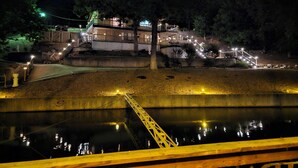 A nighttime view of a waterfront property with a bridge leading to a building with multiple levels and outdoor lighting. - Lakefront Home with Private Dock, Water Slide, Boat Slip, and Hot tub (Lake Ozark)