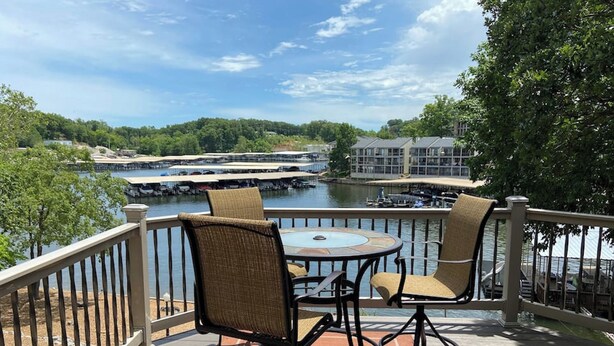 A deck with two wicker chairs and a small table, overlooking a river with boats and buildings in the background. - Lakefront Home with Private Dock, Water Slide, Boat Slip, and Hot tub (Lake Ozark)