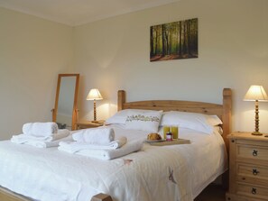 Un lit bien fait, avec des serviettes pliées, une table de chevet avec une lampe et un tableau représentant une forêt accroché au mur.