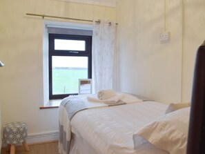 Une chambre avec un lit, une fenêtre donnant sur la mer, un petit tabouret et une prise électrique au mur.
