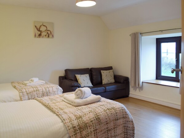 A room with two beds, a sofa, a window with curtains, and a painting on the wall.
