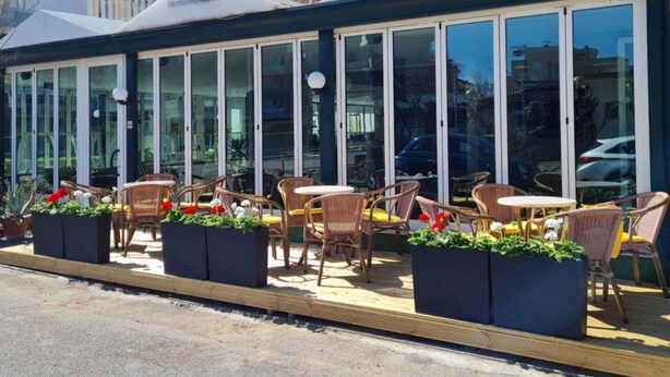 Un restaurante frente al mar con terraza, ventanas amplias y balcón.