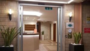 Zona de recepción con puerta de cristal, mostrador y plantas en macetas.