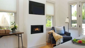 A modern living room with a fireplace, a sofa, a coffee table with fruit, and a TV mounted on the wall. - The Atlas Calistoga - Cottage #2 (Calistoga)