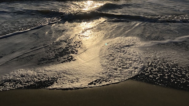 Een strand met golven en zonlicht dat op het zand schittert.